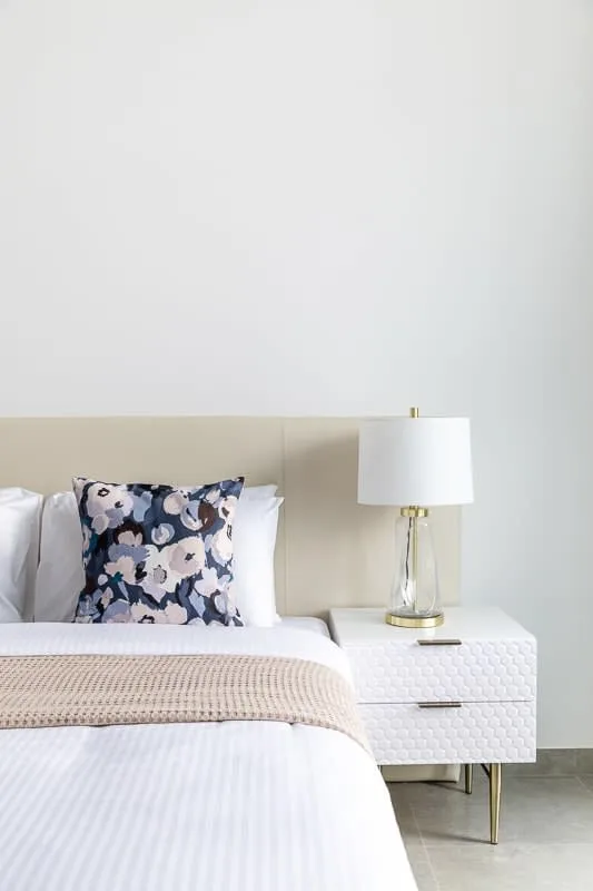 Un dormitorio con una cama ordenada, cojines estampados y una lámpara de noche.
