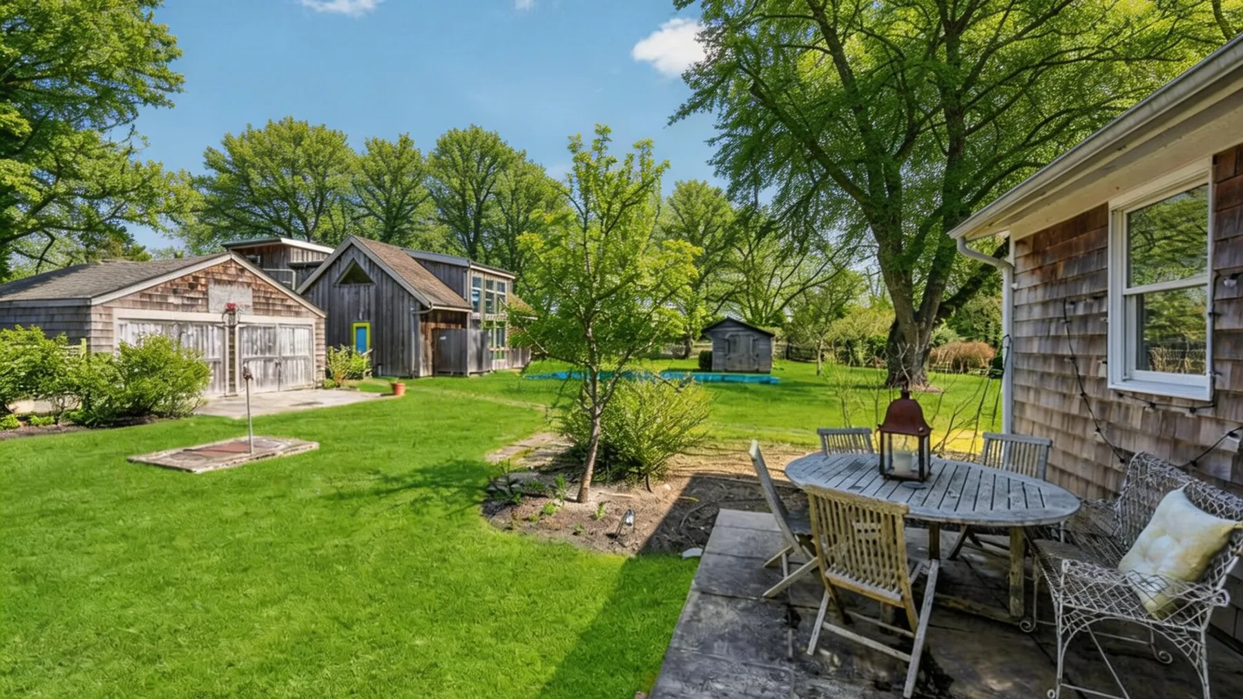 Un patio soleado con zona de estar junto a una casa y otras construcciones.