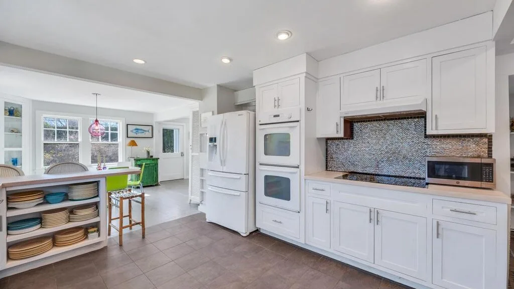 Una cocina luminosa con gabinetes blancos, refrigerador y barra para desayunar.