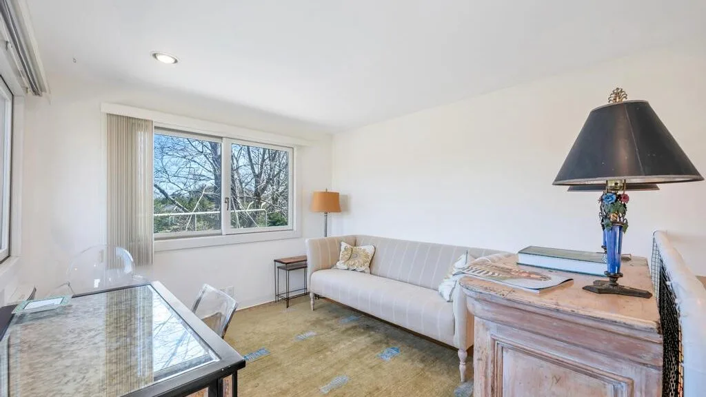Una sala luminosa con un sofá blanco, una mesa de centro de vidrio y ventanas grandes.
