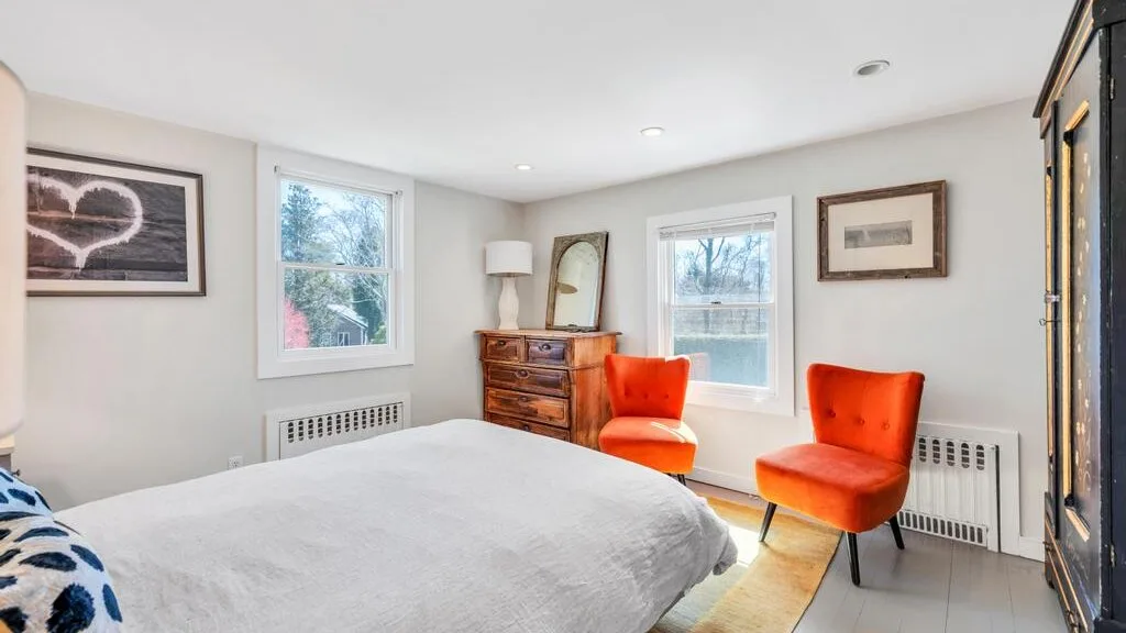 Un dormitorio luminoso con una cama tendida y asientos naranjas.