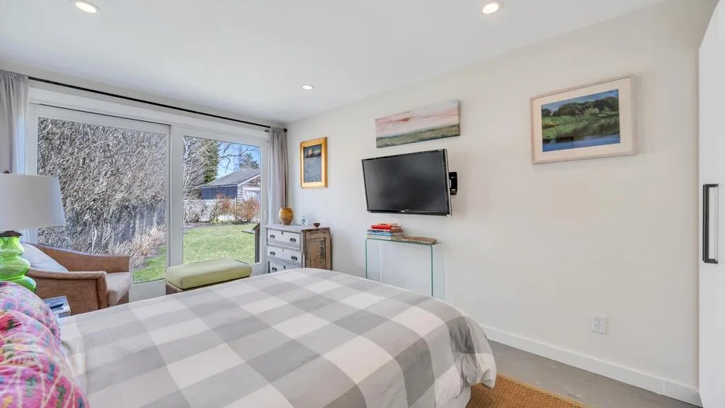 Un dormitorio con una cama grande frente a un televisor montado en la pared y puertas corredizas de vidrio.