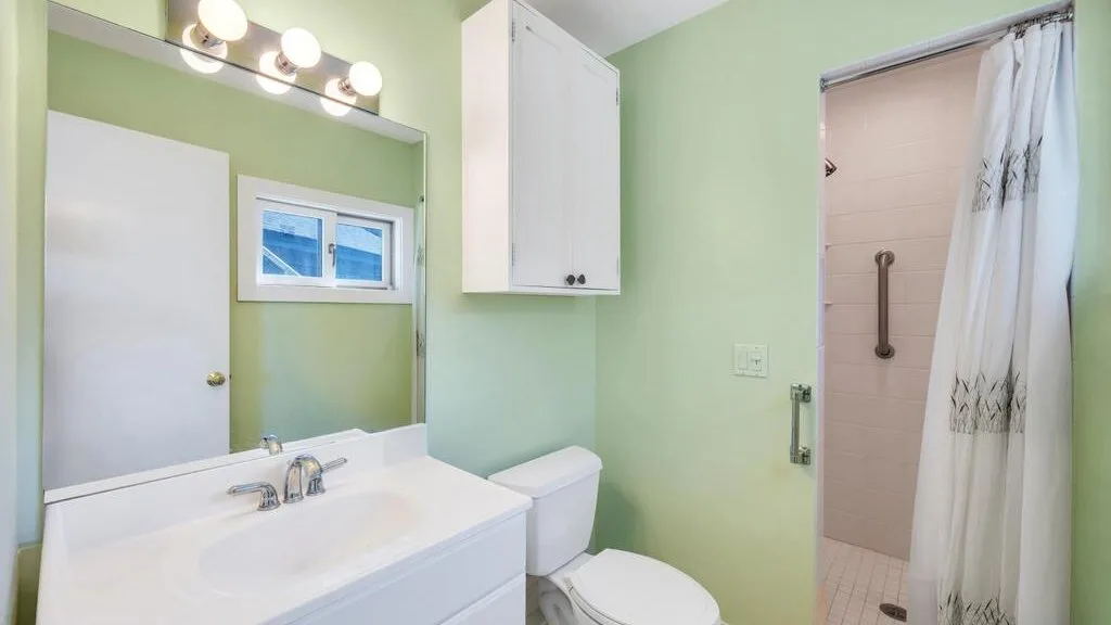 Un baño verde con lavabo blanco, inodoro y cortina de ducha abierta.