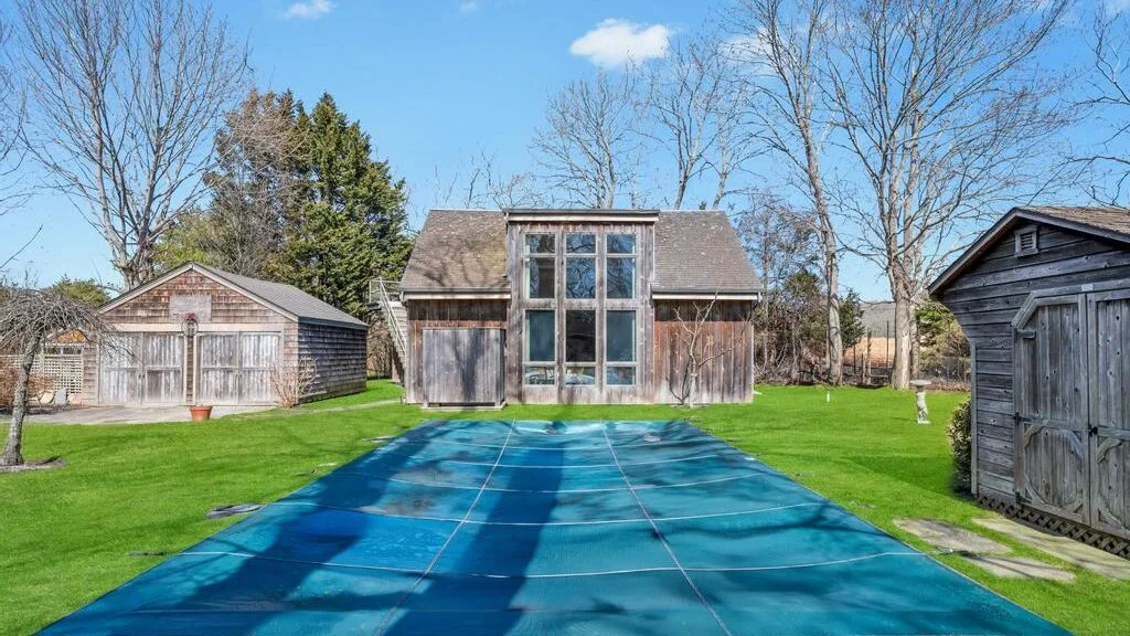 Una piscina trasera cubierta con una lona azul, con una casa y cobertizos al fondo.