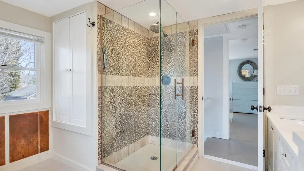 Un baño luminoso con una ducha de vidrio y una ventana.