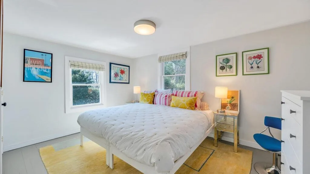 Un dormitorio luminoso con una cama grande, almohadas coloridas y cuadros en la pared.