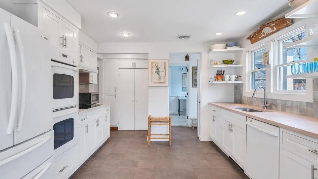 Una cocina luminosa con gabinetes blancos y un pasillo central de baldosas.