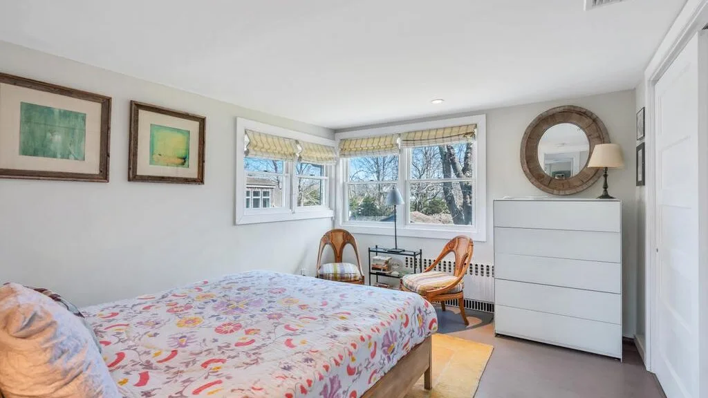 Un dormitorio luminoso con una colcha estampada y ventanas con vistas a los árboles.