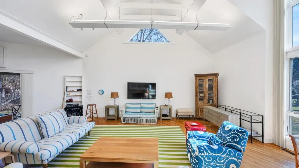 Una sala luminosa con una alfombra a rayas, asientos y un televisor en la pared.