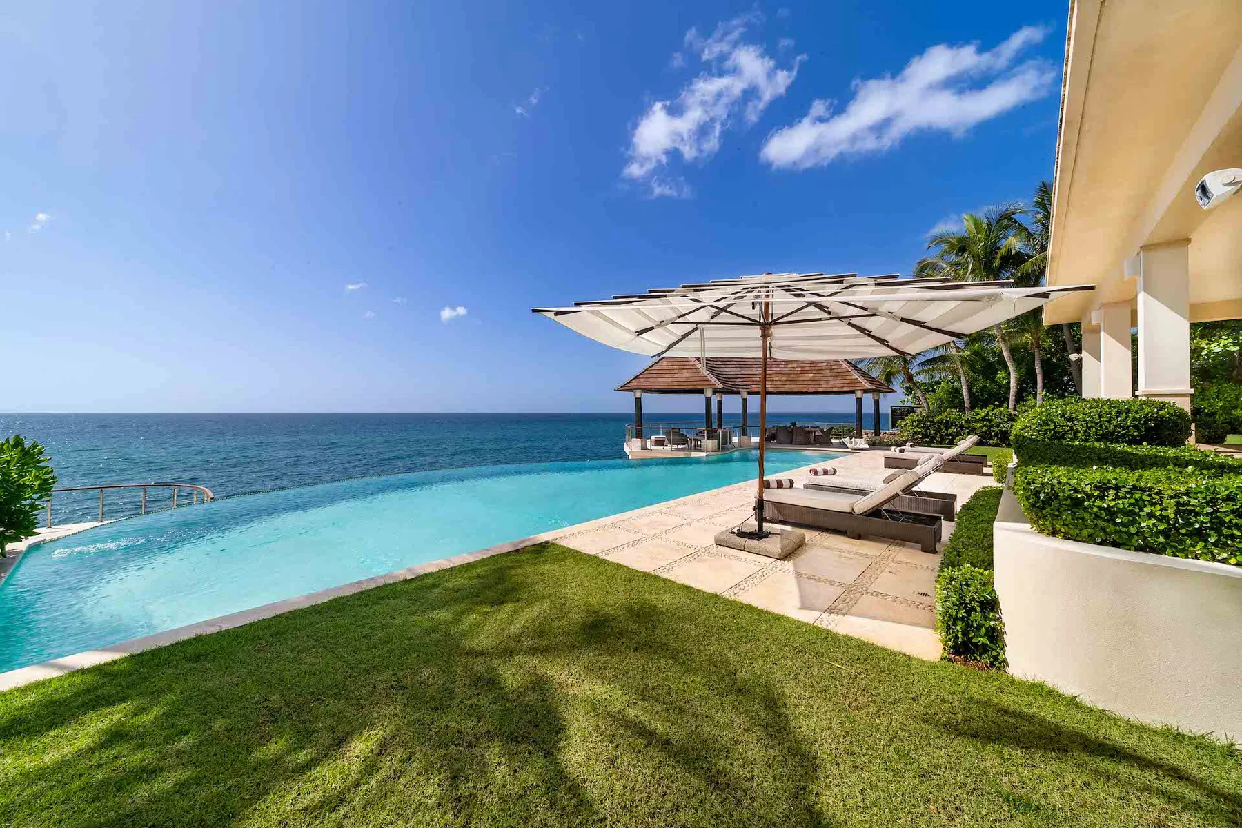 An outdoor poolside patio overlooks the sea, with shaded seating beside the water.