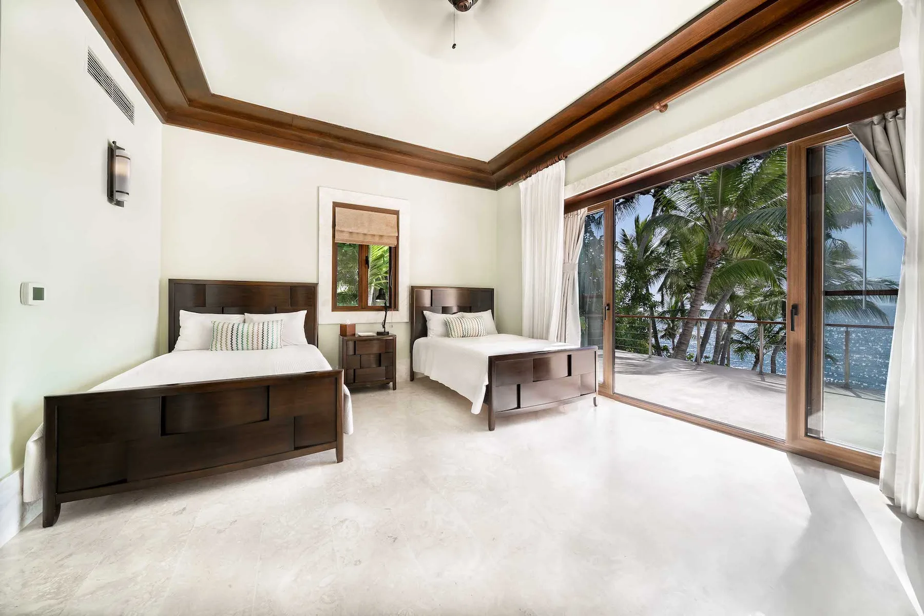 A bright bedroom with two beds and sliding glass doors opening onto a tropical view.