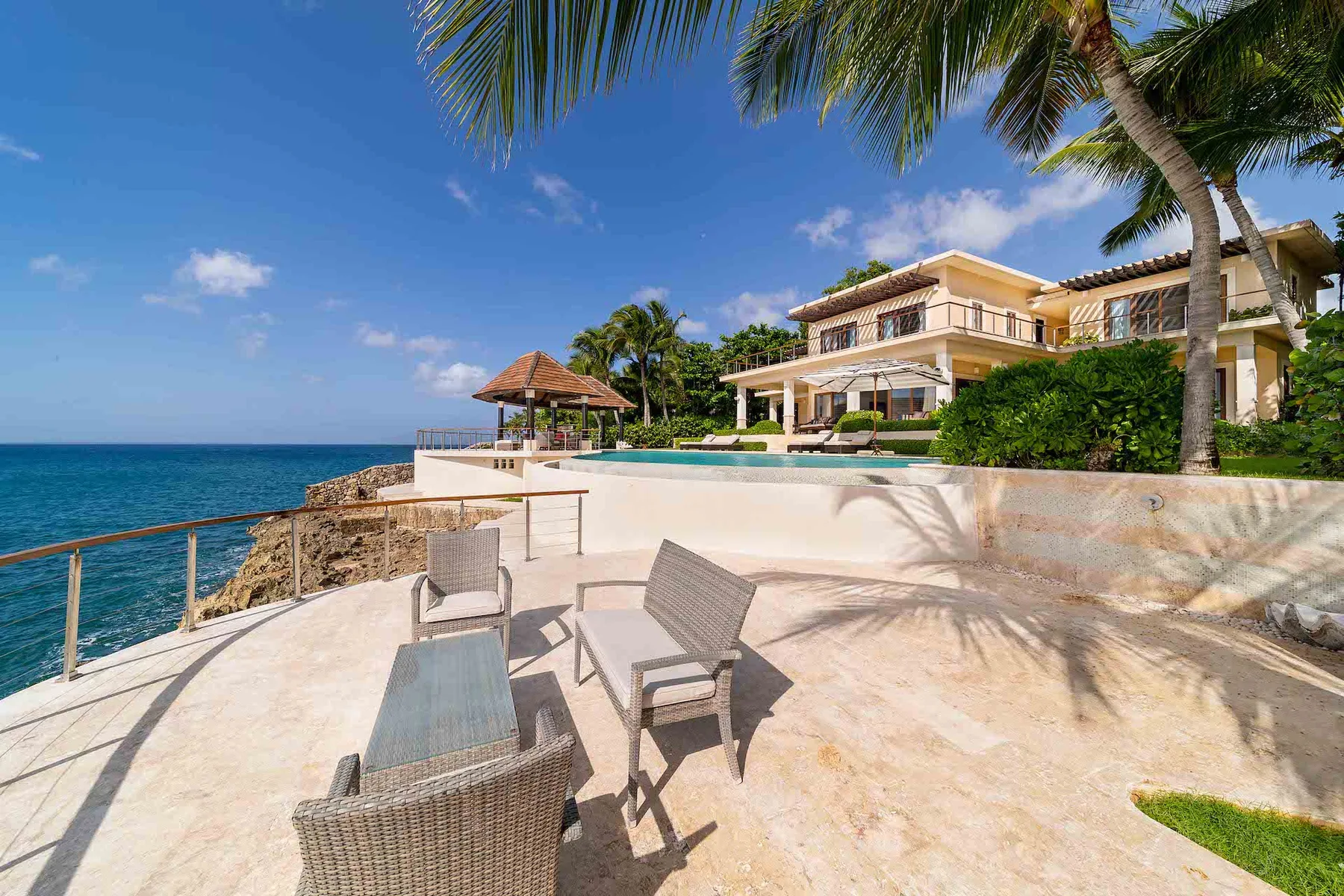 A seaside patio with outdoor seating overlooks the ocean and a pool.