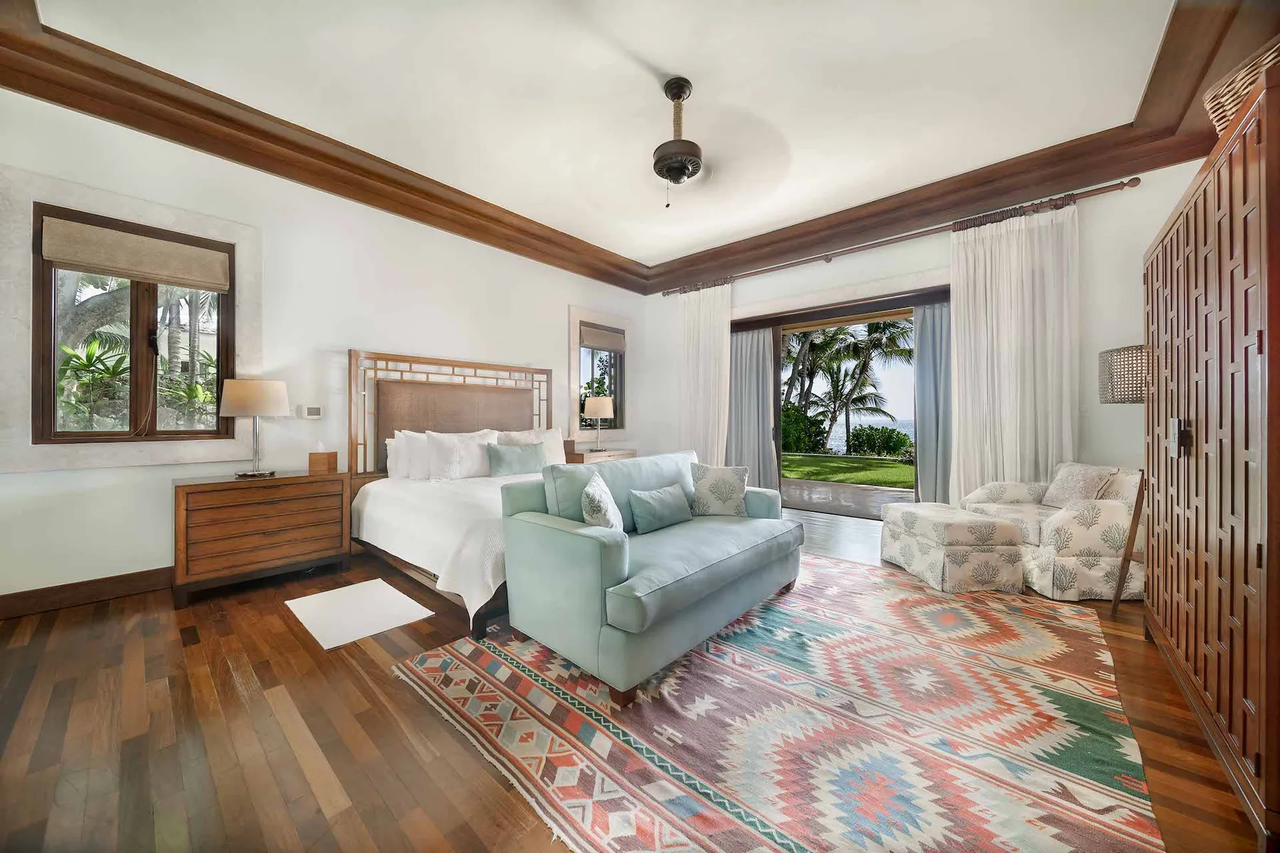A bedroom with a bed, seating, and a large window overlooking tropical greenery.
