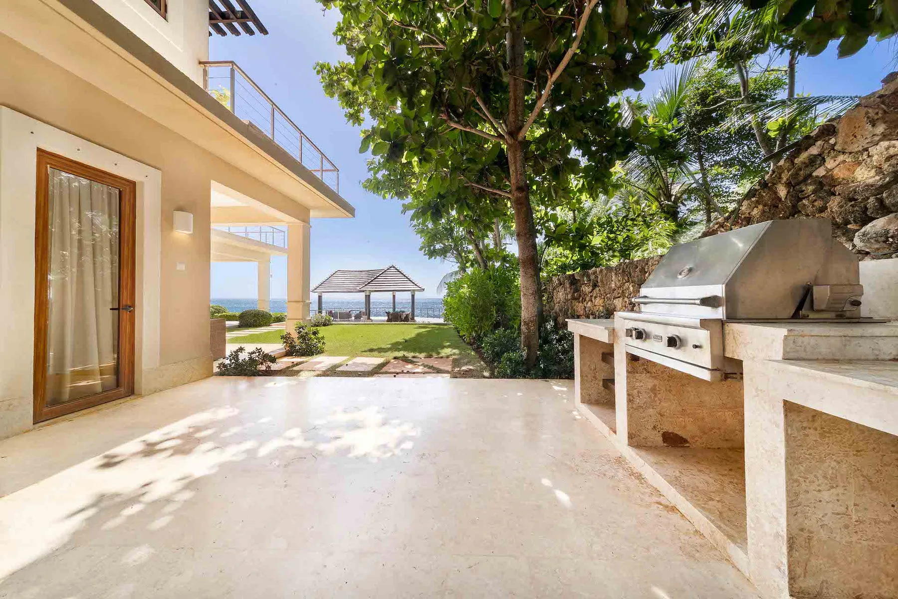 An outdoor patio with a built-in grill beneath a leafy tree.