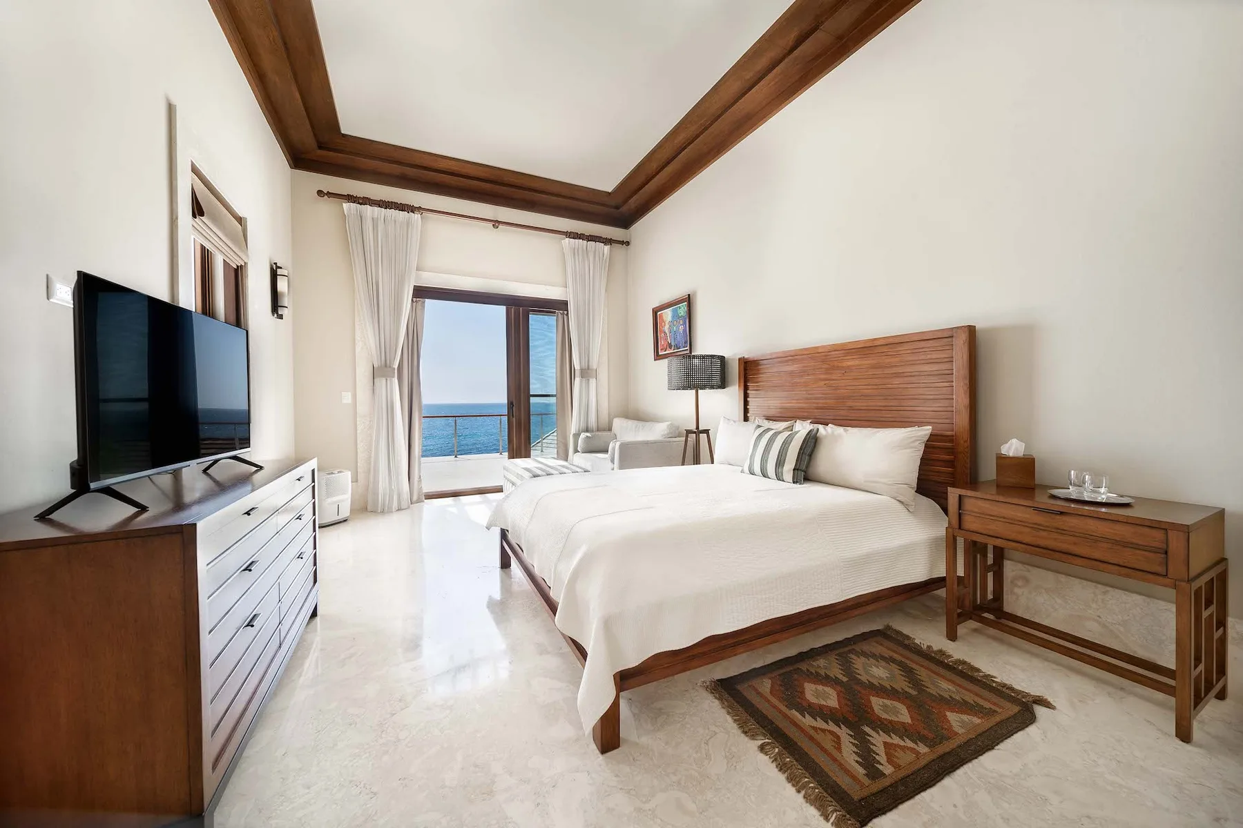A bright bedroom with a large bed and ocean views through the balcony doors.