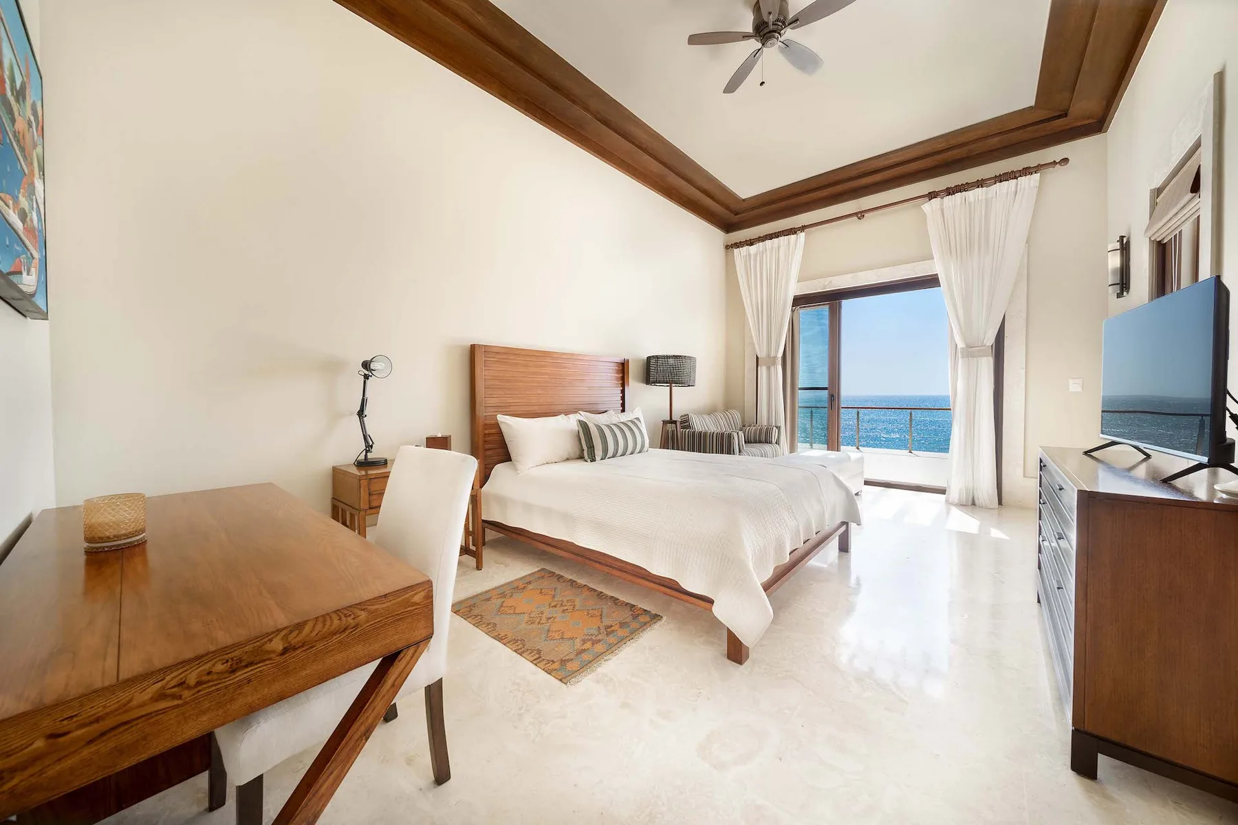 A bedroom with a bed, desk, and open curtains overlooking the water.