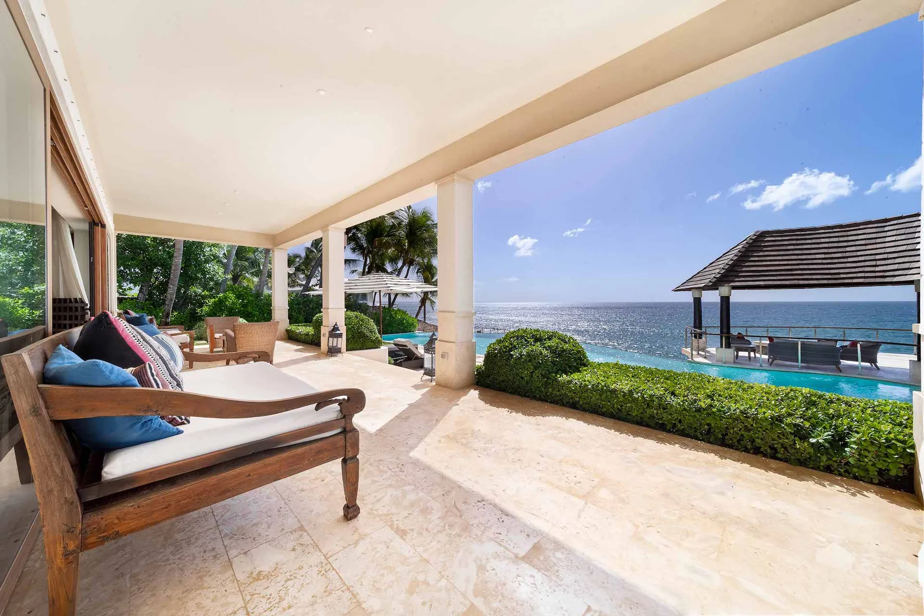 A covered seaside patio with cushioned seating and a view of the water.