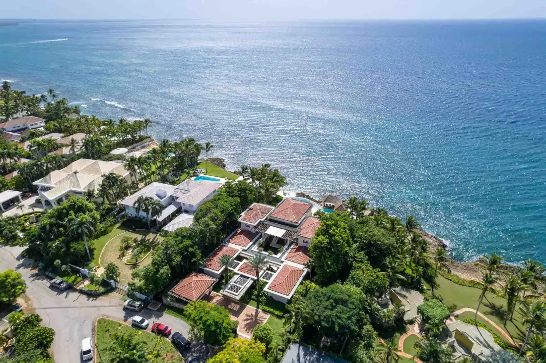 Aerial view of coastal homes and gardens beside the ocean.