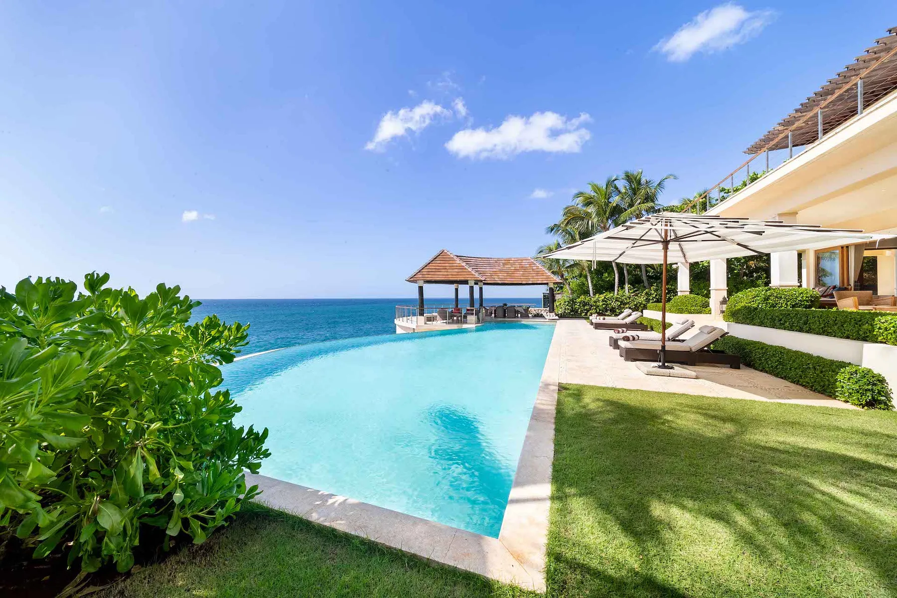 An outdoor pool beside the ocean, with shaded loungers along the deck.