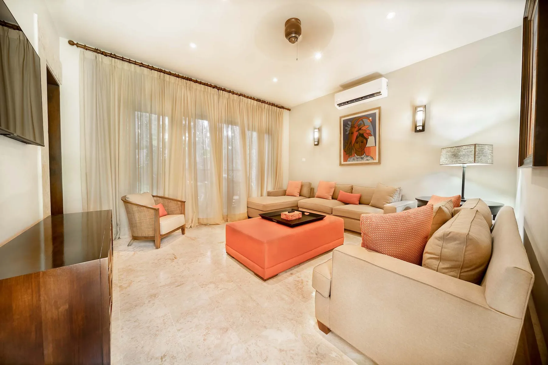 A bright living room with seating around a large orange ottoman.