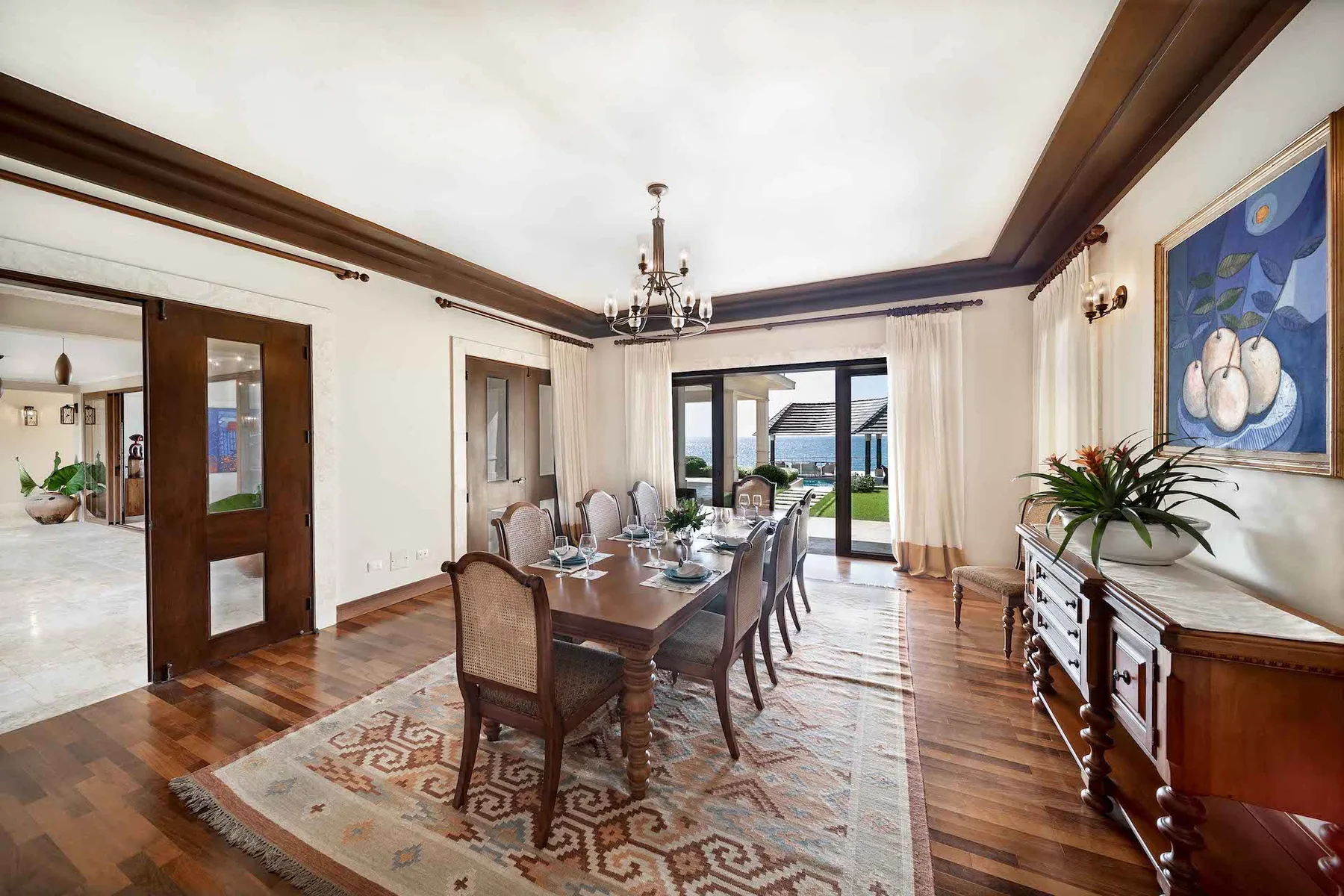 A dining room with a long table and chairs beside glass doors opening onto a patio.