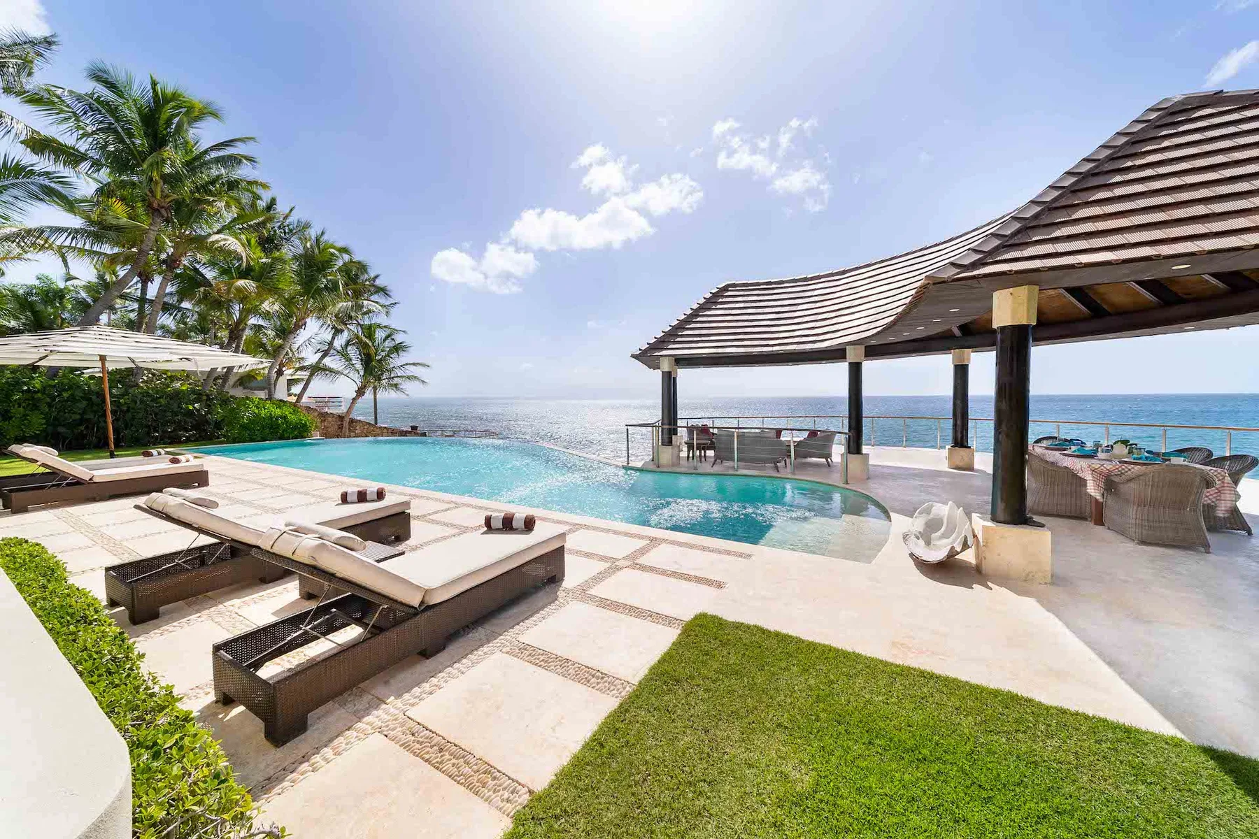Un patio junto a una piscina al aire libre, con asientos, palmeras y vistas al mar.