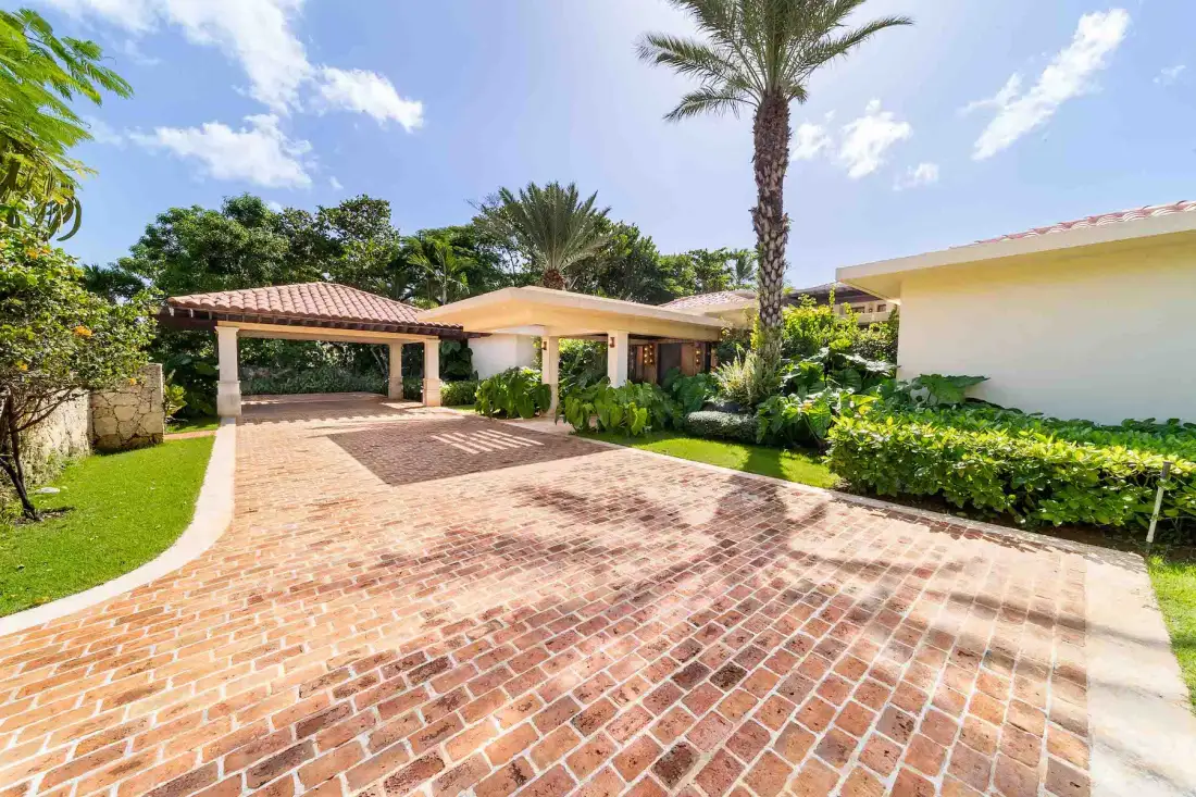 A brick-paved driveway leads to a covered carport beside a landscaped house.