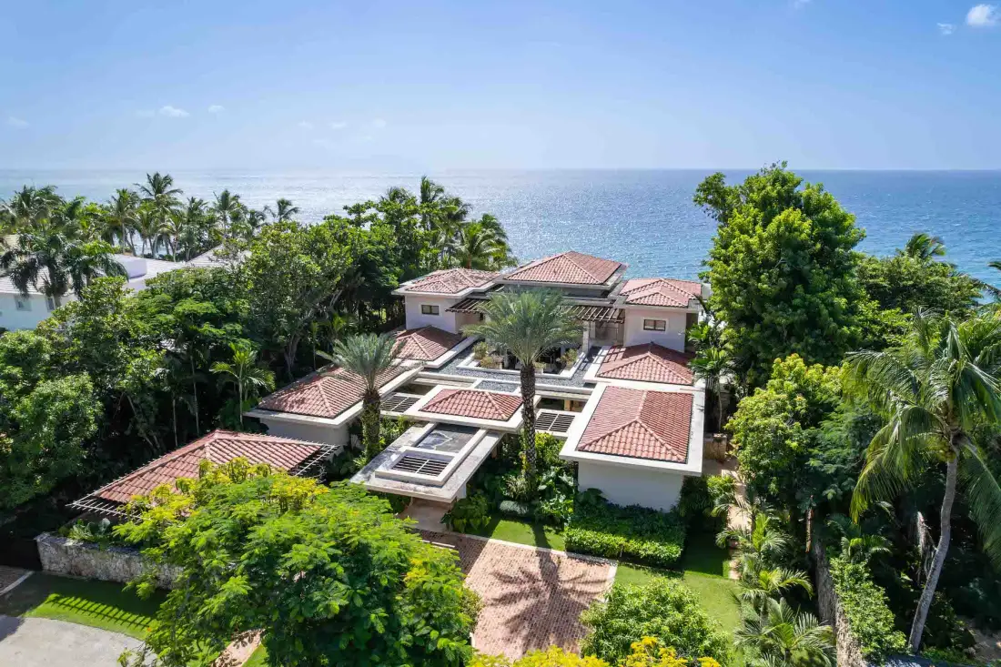 A tropical resort complex sits among lush greenery beside the ocean.
