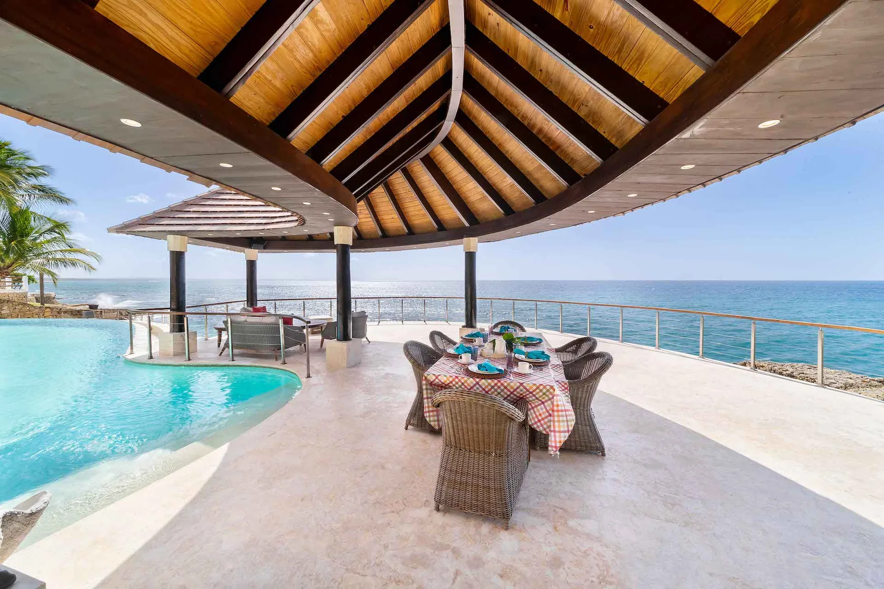 A covered dining area beside a pool overlooks the ocean.