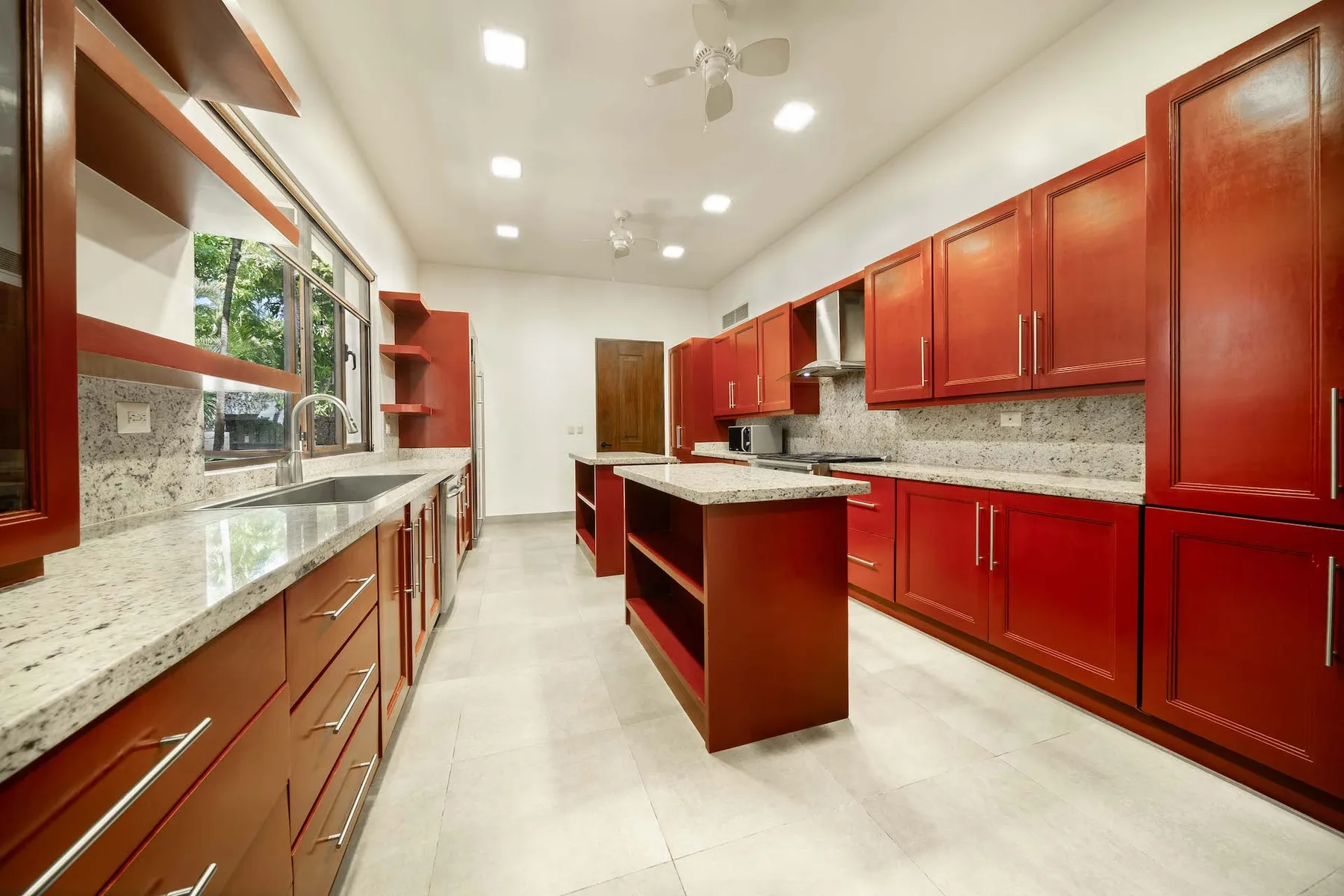 A bright kitchen with red cabinets, stone counters, and a central island.