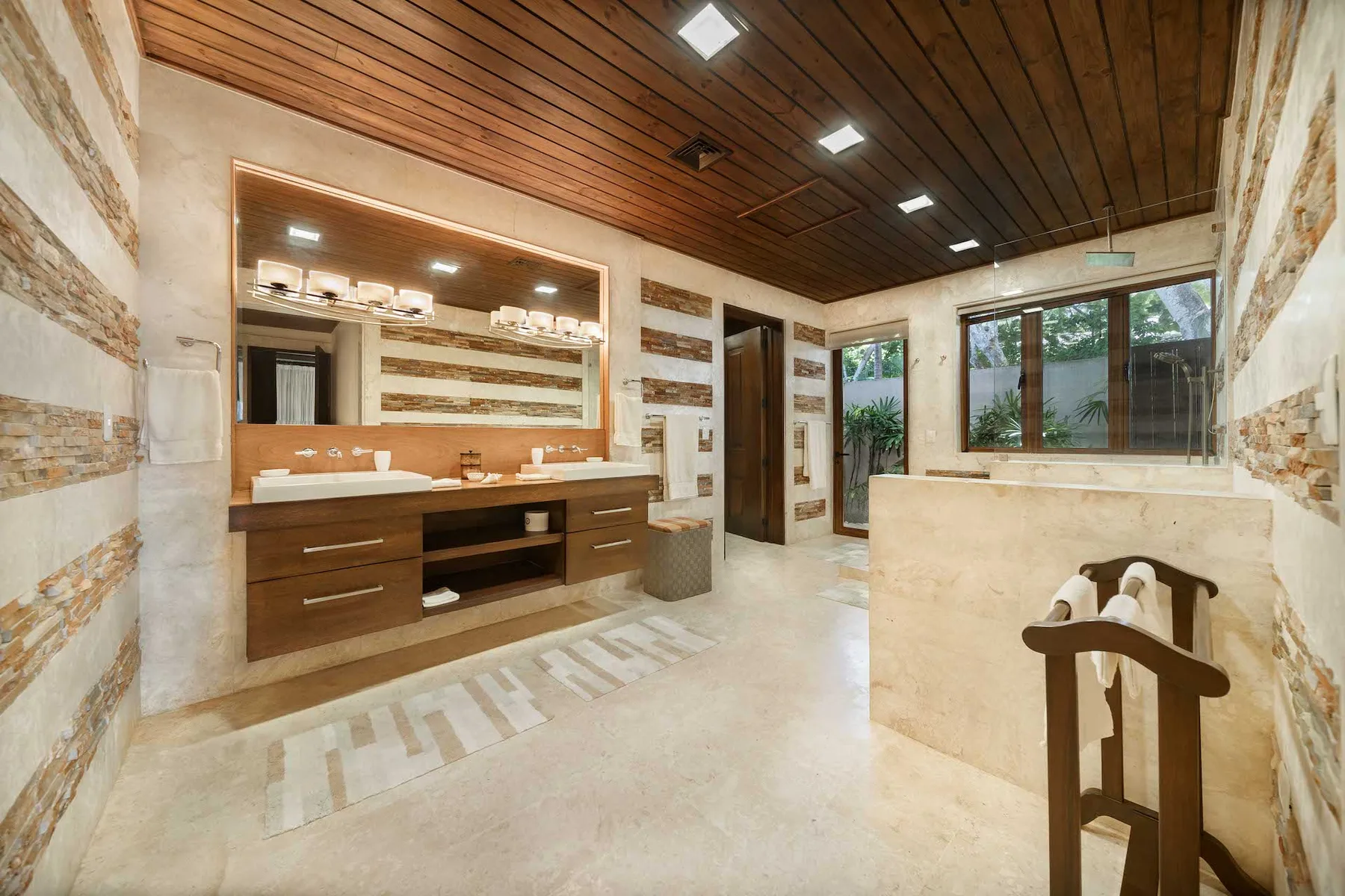 A bathroom vanity and sink sit beneath a large mirror, with a window nearby.