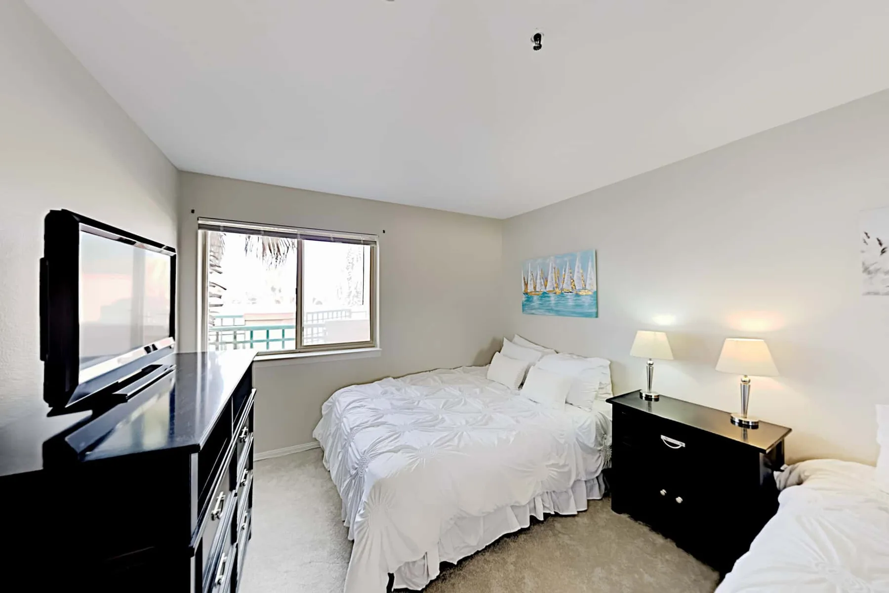 Un dormitorio luminoso con ropa de cama blanca, un televisor y una ventana.