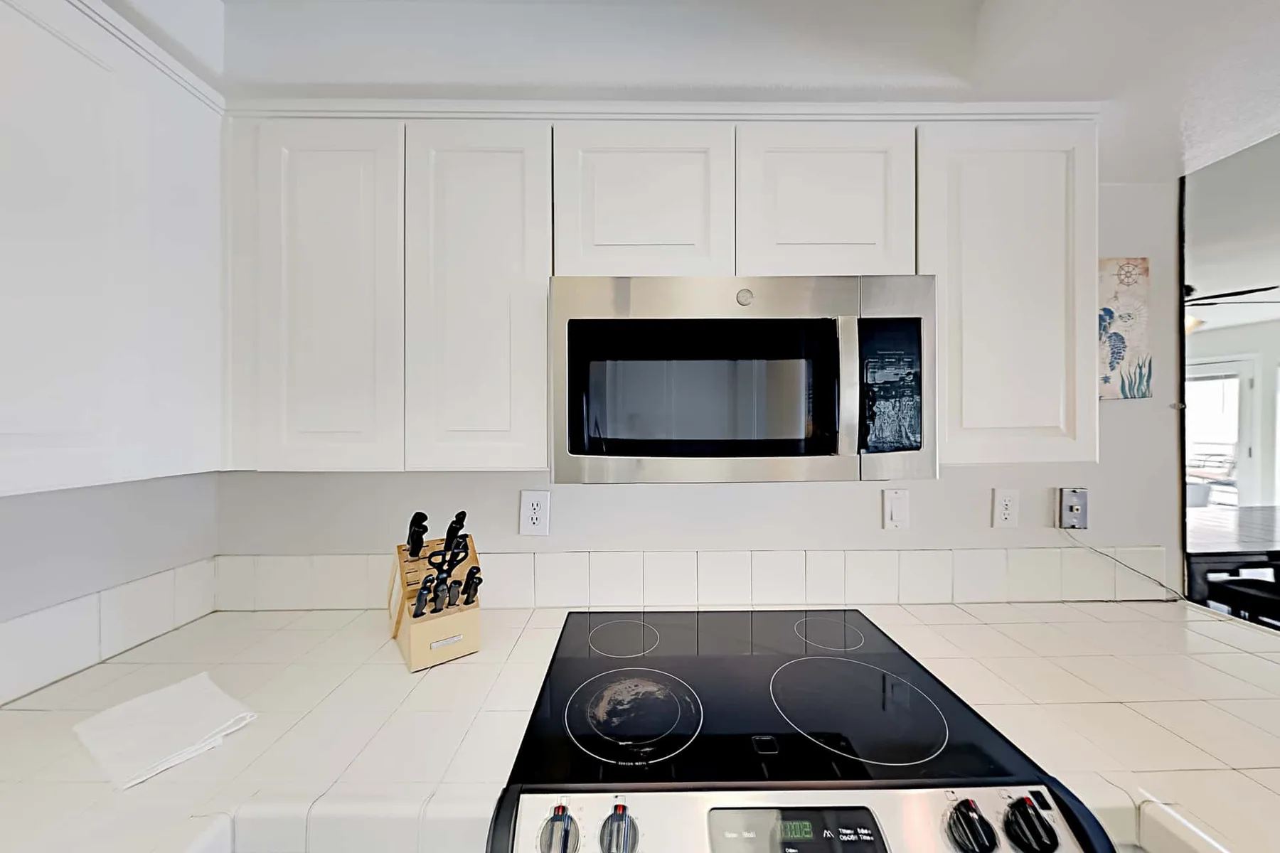A bright kitchen with white cabinetry, a microwave, and a cooktop.