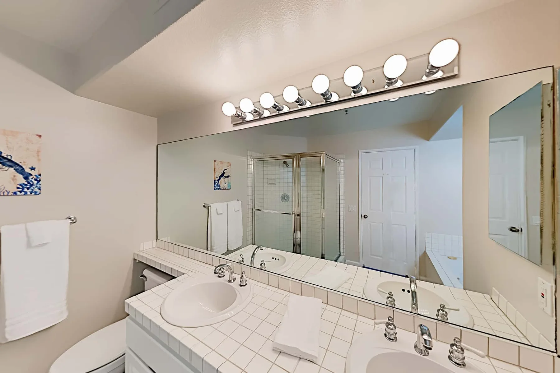Un lavabo de baño con un espejo amplio y una ducha al fondo.