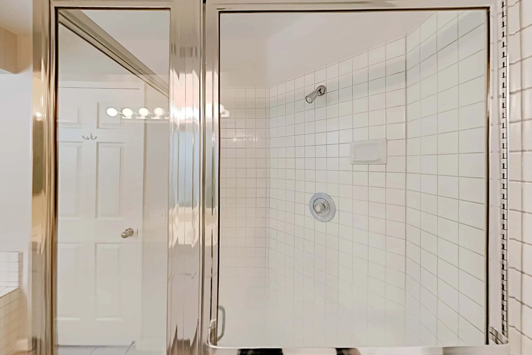 Una zona de ducha con azulejos, puerta de vidrio y accesorios en la pared.
