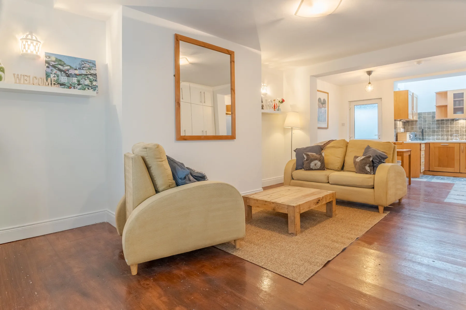 Sala de estar con asientos beige, una mesa de centro de madera y una cocina abierta.