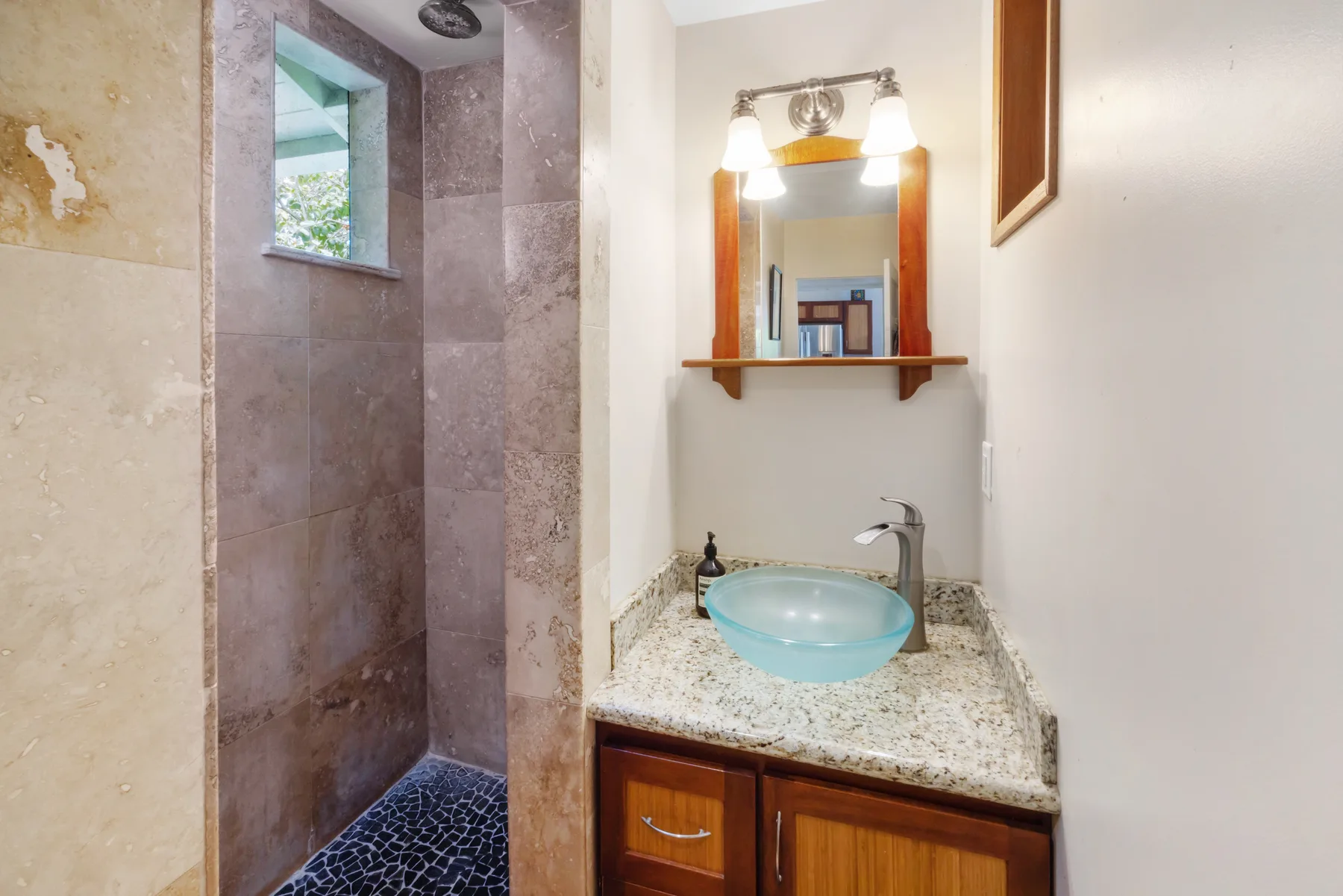 A bathroom with a tiled shower and a vanity topped by a blue basin.