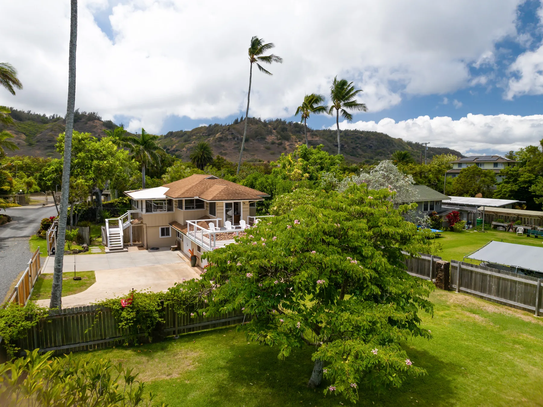 A residential neighborhood with a house, green lawns, and hills in the background.