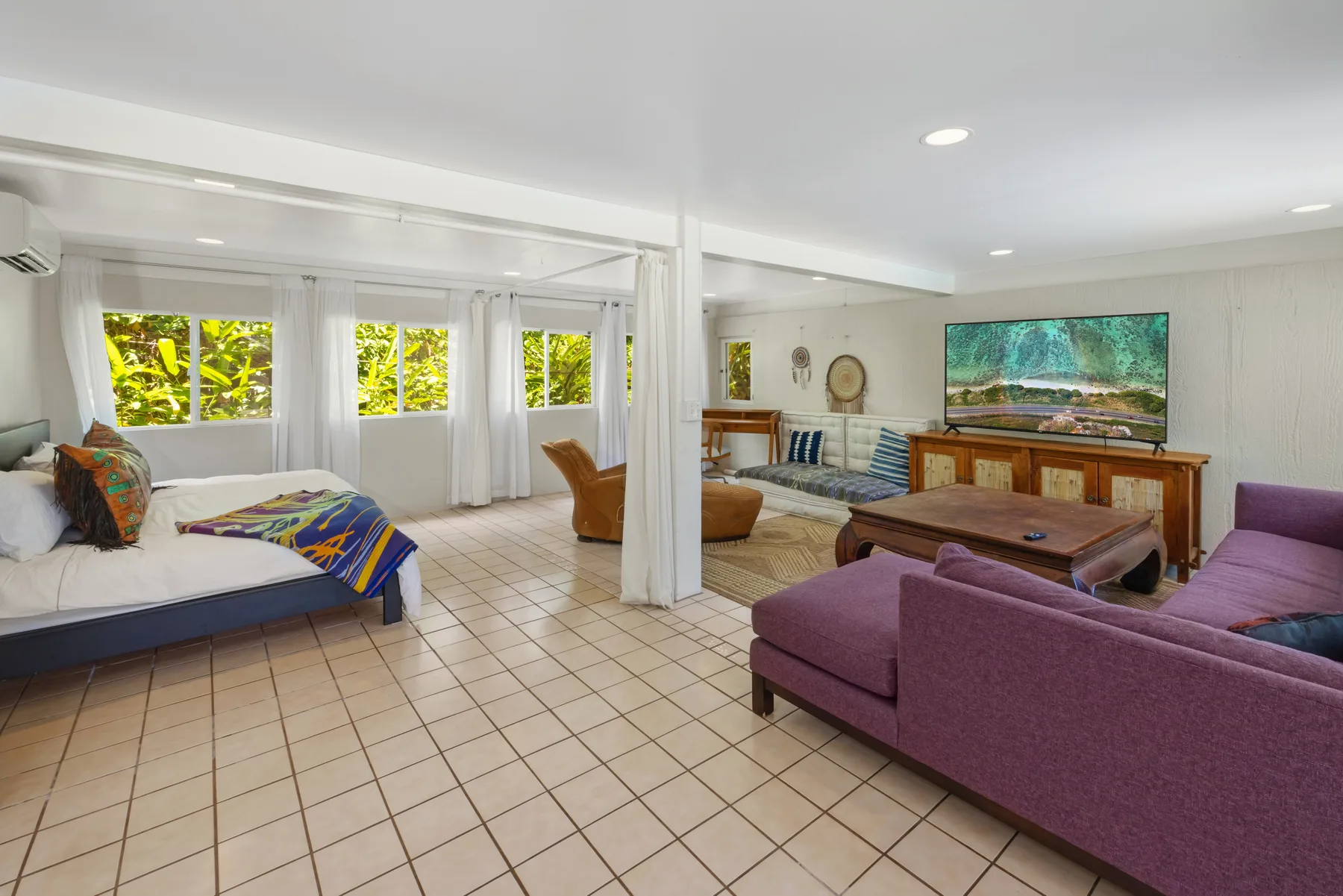 A bright open-plan living room with a bed, seating, and large windows.