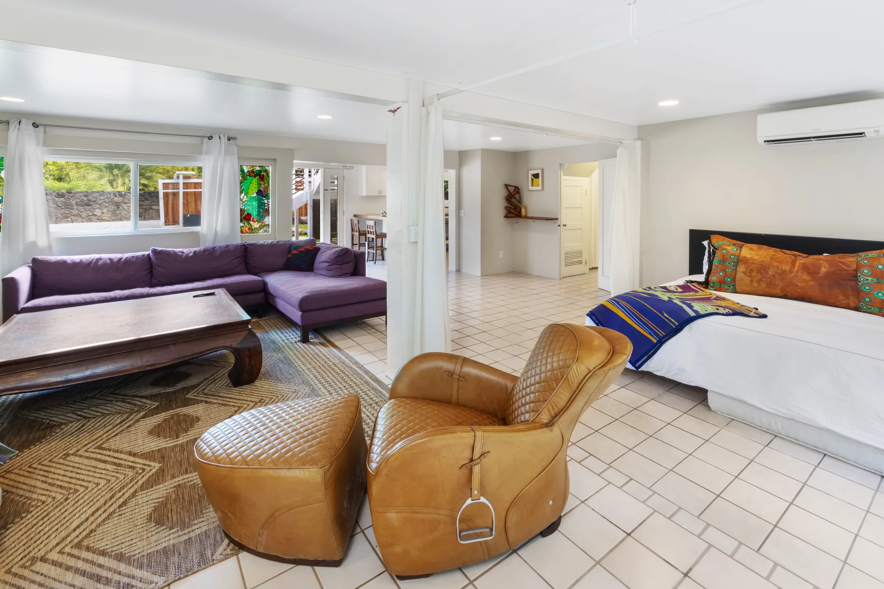 A bright open-plan room combines a living area with a bed and tiled flooring.
