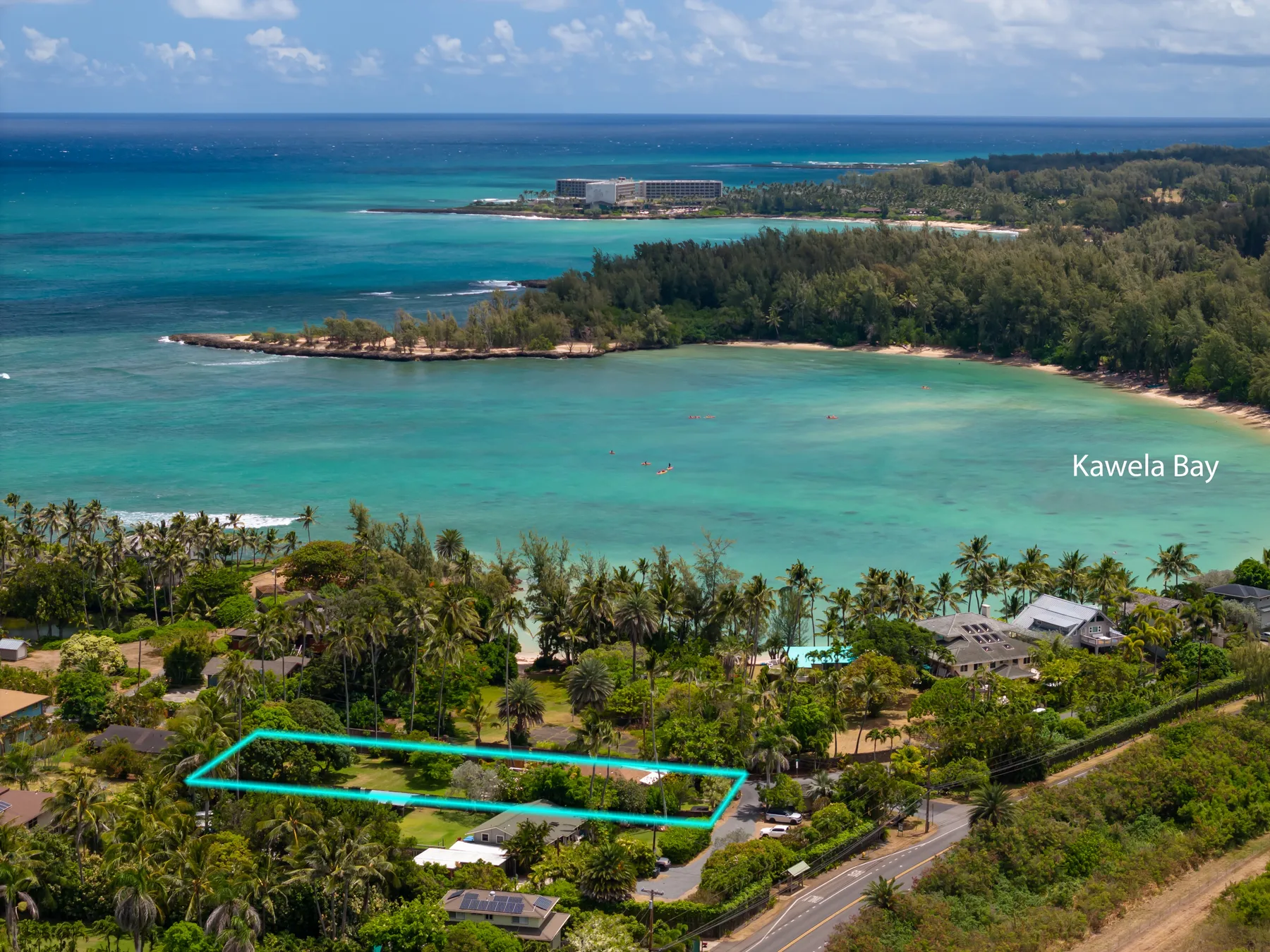 An aerial view of a tropical bay with turquoise water and a palm-lined shore.