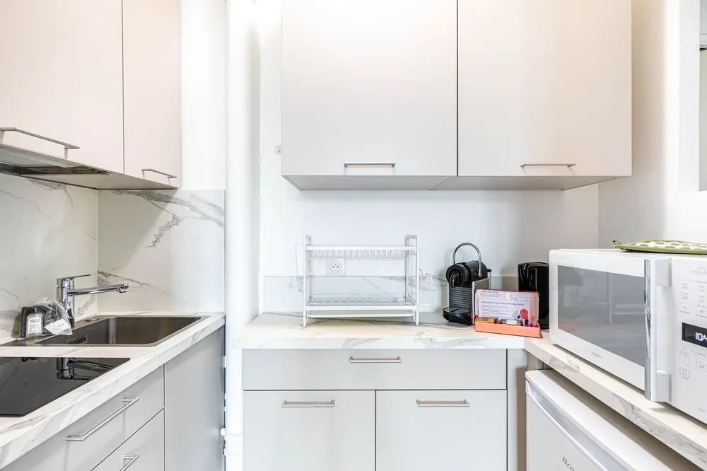 A bright kitchen with white cabinets, a sink, and countertop appliances.