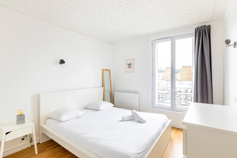 A bright bedroom with a neatly made bed beside a large window.
