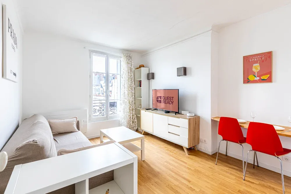 A bright living room has a sofa, coffee table, and television beside a dining area.
