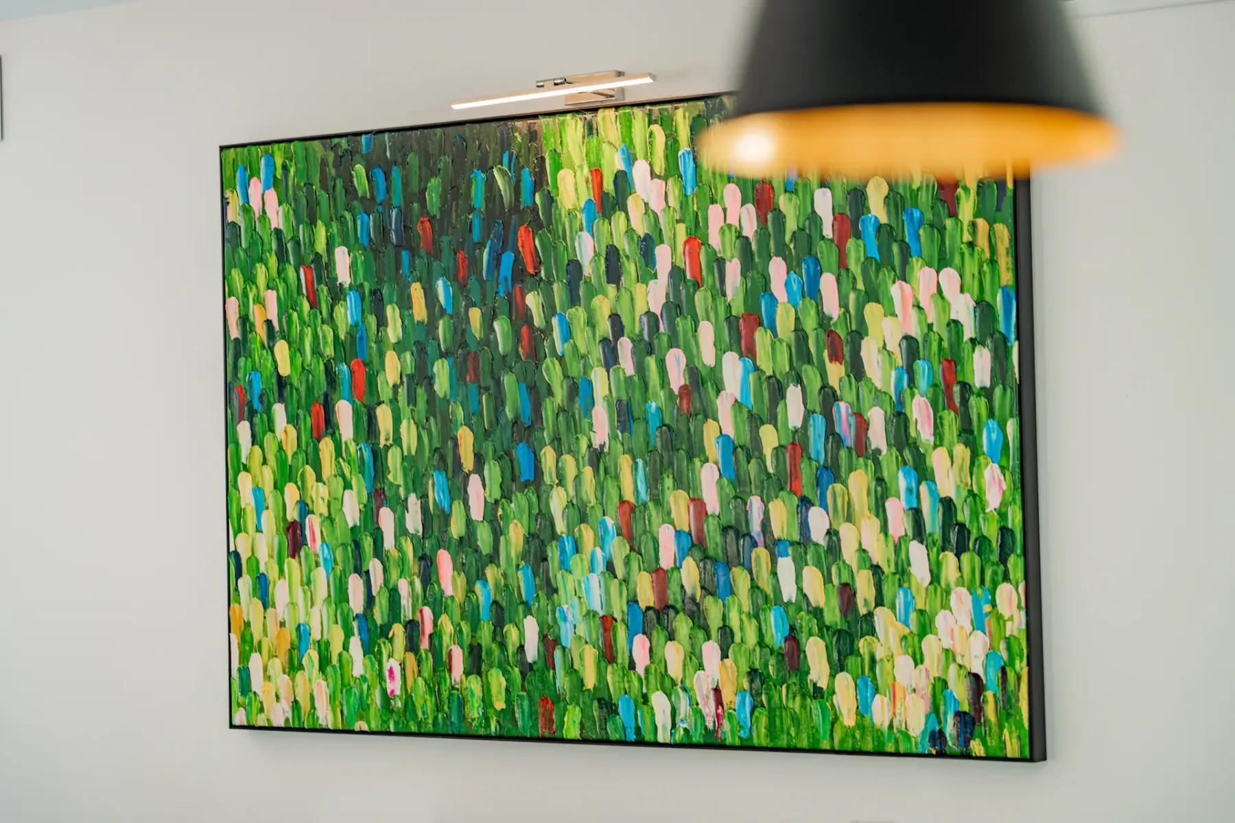 Un colorido cuadro abstracto con trazos cortos verdes, azules, amarillos y rosas cuelga en una pared.