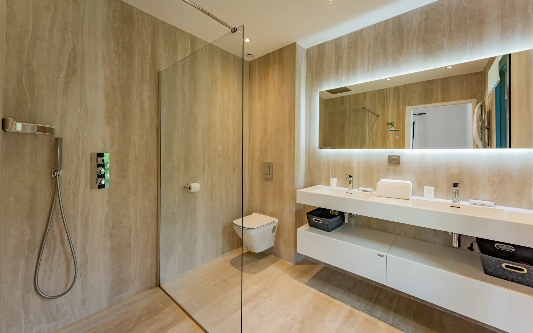 Baño moderno con ducha de vidrio, inodoro suspendido y espejo iluminado.