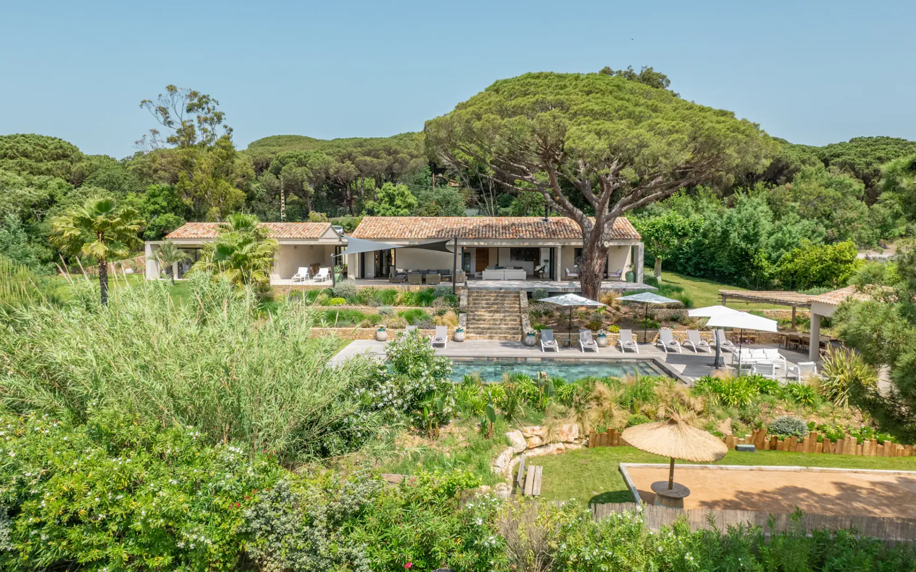 Una villa está rodeada de vegetación densa, con una piscina y asientos al aire libre.
