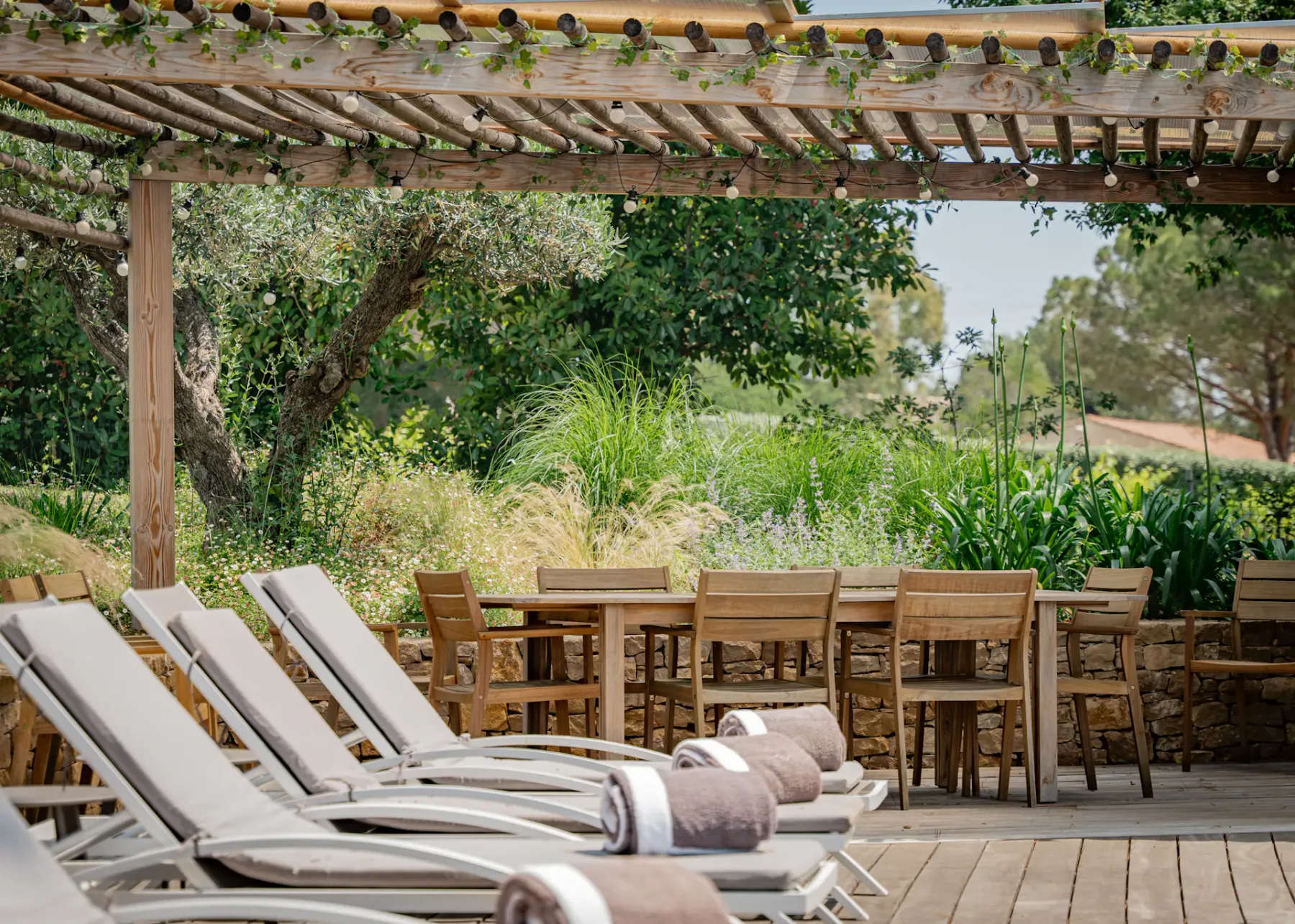 Un patio al aire libre con tumbonas y una mesa de comedor de madera bajo una pérgola.