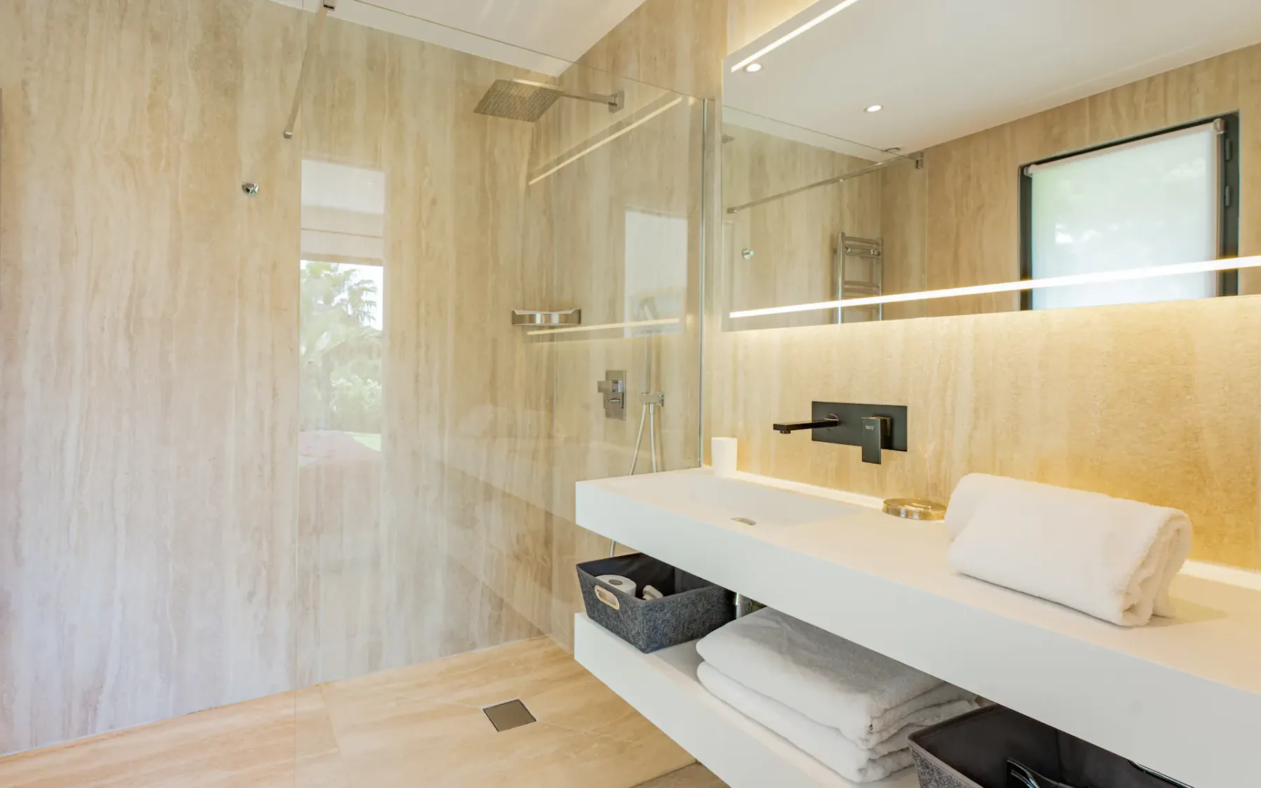 Un baño moderno con ducha, un lavabo blanco alargado y una ventana.