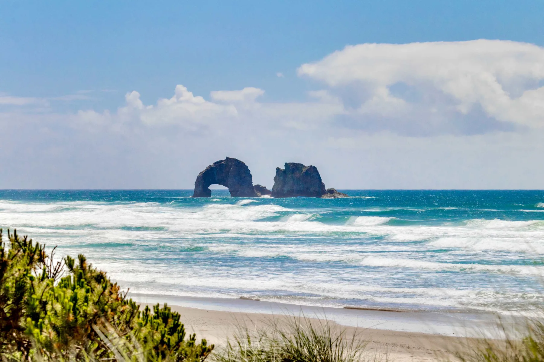 Una playa de arena con olas rompiendo junto a formaciones rocosas mar adentro.